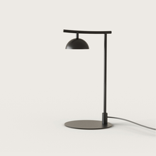 Lámpara de escritorio minimalista de color negro, con cuello curvo y pantalla en forma de cúpula, colocada sobre una superficie blanca con un cordón visible. Esta Lámpara de mesa Tana presenta elementos de diseño moderno para una apariencia atractiva.