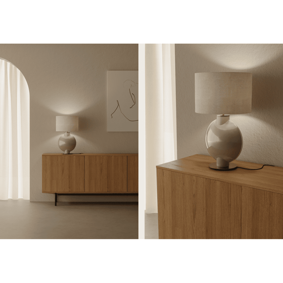 Interior minimalista con aparador de madera, Tilla lámpara de mesa y arte abstracto en la pared en una habitación con iluminación tenue y puerta arqueada.