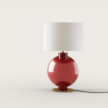  Una moderna Lámpara de mesa Tilla con una base roja brillante y un diseño circular, complementada por una simple pantalla blanca, mostrada sobre un fondo blanco liso.