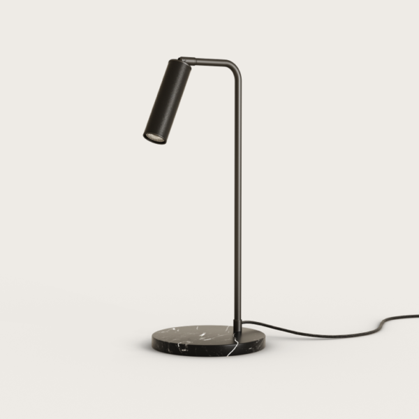La lámpara de mesa Tura presenta un elegante cabezal cilíndrico negro sobre un tallo curvo, colocado sobre una base redonda de mármol, mostrando un diseño contemporáneo con su cable visible cuando está enchufado.
