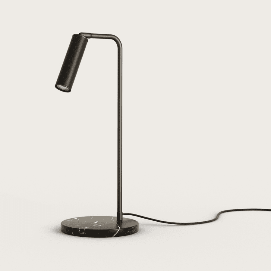 La lámpara de mesa Tura presenta un diseño moderno y elegante en color negro, con una pantalla cilíndrica sobre una base redonda de mármol unida por una varilla fina. Fabricada con materiales de alta calidad, su aspecto elegante se complementa con un cable eléctrico que se extiende desde la base.