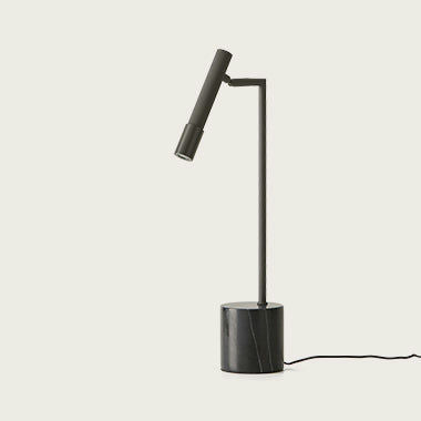 La lámpara de mesa Ycro en color negro cuenta con un diseño elegante y minimalista con una base cilíndrica y un brazo ajustable, proporcionando una iluminación funcional que se alimenta fácilmente mediante un cable.