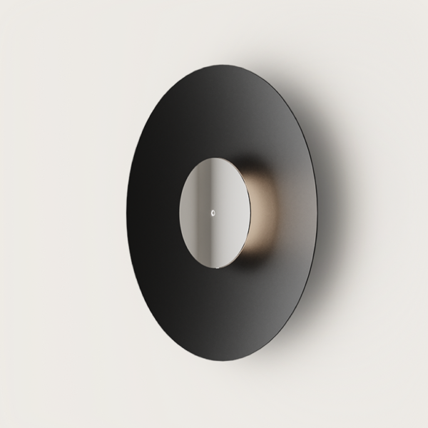 La lámpara de pared BigCoss es una lámpara de pared circular de color negro con un espejo central y una suave iluminación indirecta que proyecta un brillo ambiental sobre un fondo blanco, personificando el minimalismo.