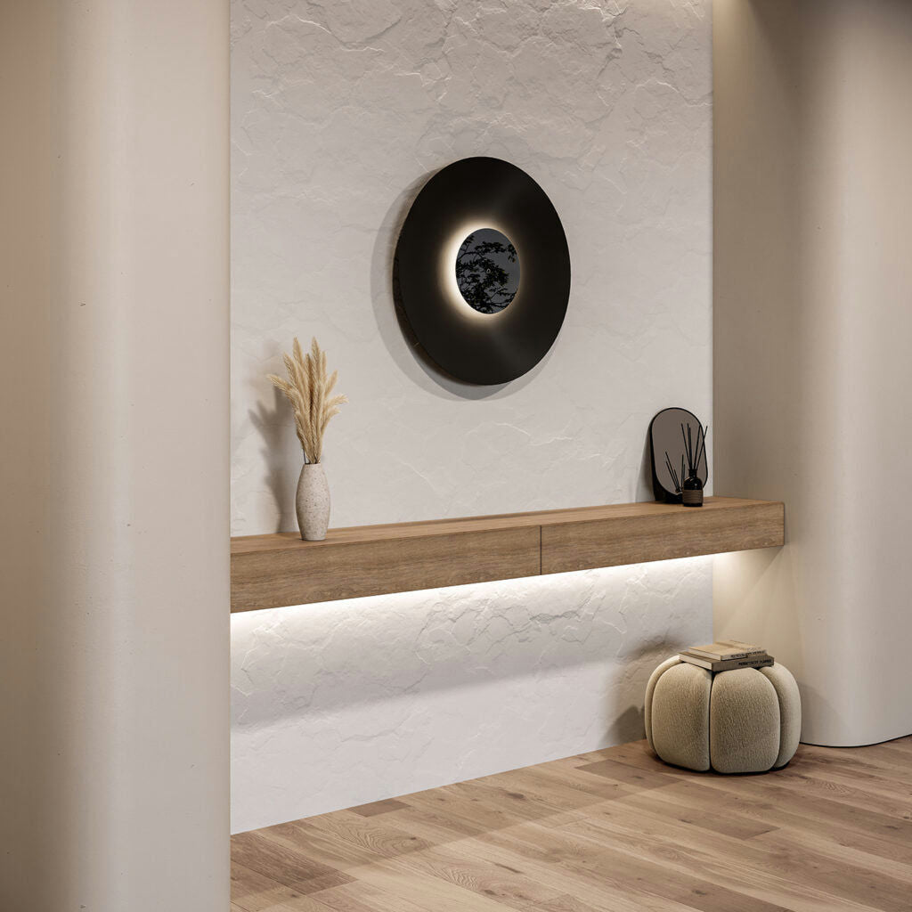 Un interior minimalista con un estante flotante de madera, jarrones decorativos y un espejo de pared circular. La lámpara de pared BigCoss aporta una suave iluminación indirecta, mientras que un taburete acolchado sobre el suelo de madera completa el diseño minimalista.