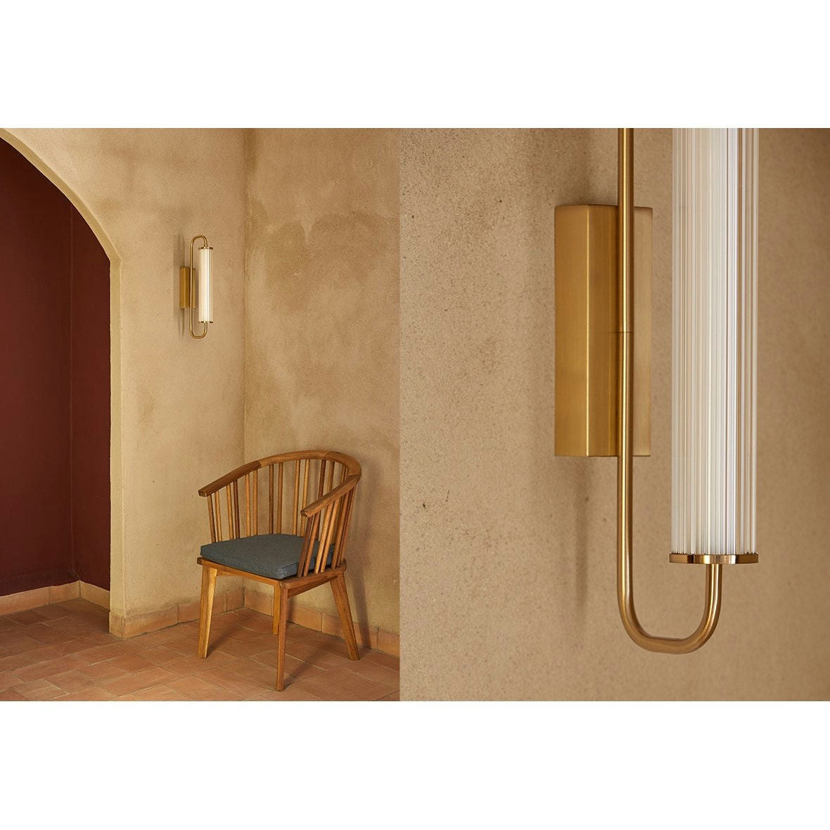 Una silla de madera con un cojín oscuro se apoya contra una pared beige que presenta una puerta arqueada y la Lámpara de pared Ison dorada vertical, agregando un toque de elegancia industrial y ofreciendo una iluminación complementaria perfecta.