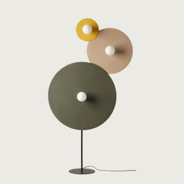 La Lámpara de pie Artic presenta un diseño atrevido y contemporáneo con tres pantallas circulares superpuestas en verde, beige y amarillo, cada una de las cuales alberga una bombilla.