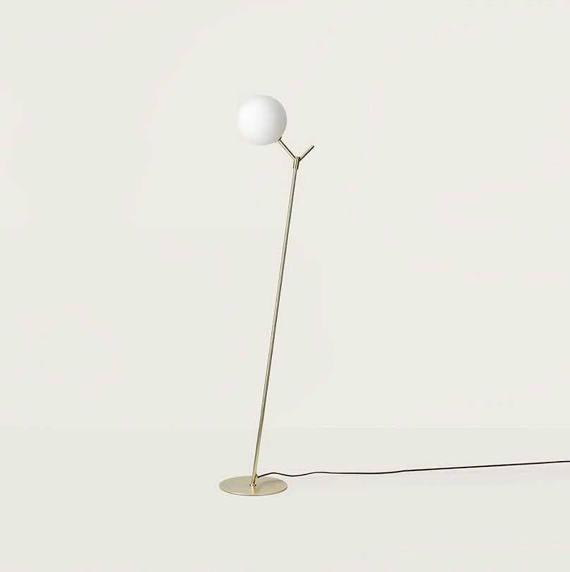 La Lámpara de pie Atom tiene una pantalla esférica blanca sostenida por un soporte de latón delgado y angular sobre una base circular. Ideal para iluminación de tareas, esta pieza minimalista combina funcionalidad con una elegante simplicidad en un fondo neutro.