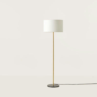 La Lámpara de pie Hedra cuenta con un diseño elegante con una pantalla cilíndrica blanca, un soporte dorado delgado y una base negra redonda, que incorpora un diseño minimalista sobre un fondo claro y sencillo.