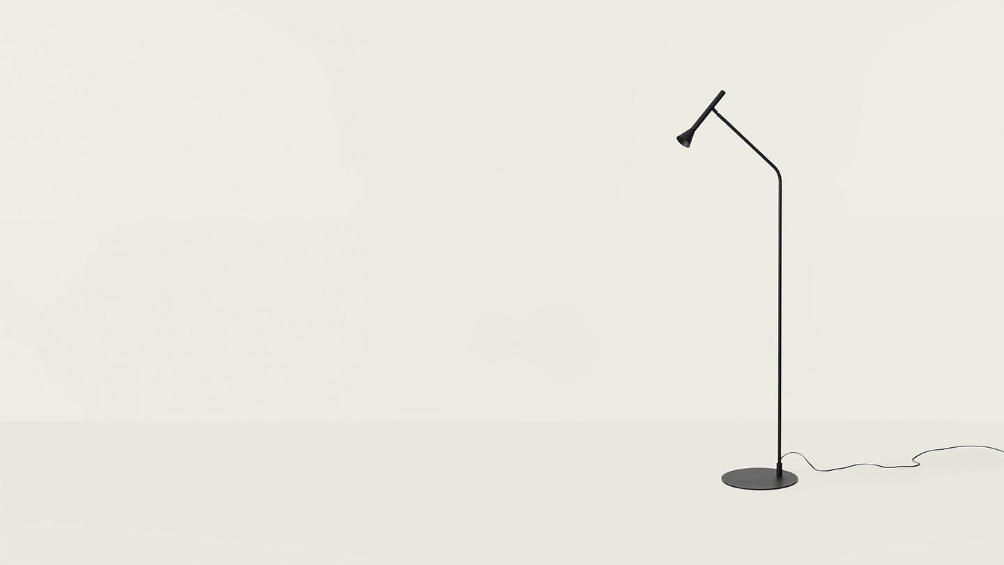 La lámpara de pie Lyb, de diseño minimalista y esbelto en color negro, es ideal para iluminación focalizada sobre un fondo blanco sencillo.