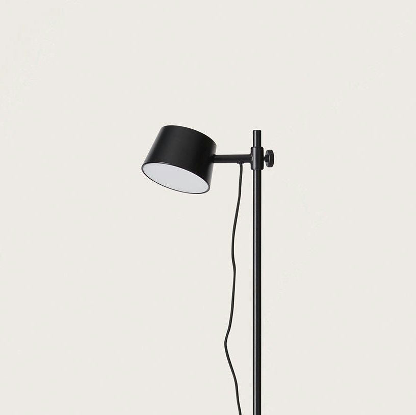 La Lámpara de pie Nera presenta una elegante cabeza cilíndrica negra con un cable visible, sobre un fondo liso para resaltar su diseño moderno.