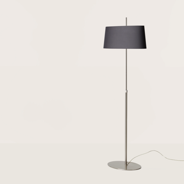 Una moderna Lámpara de pie Ona con un elegante soporte de metal y una pantalla oscura, con iluminación funcional, sobre un fondo liso y claro.