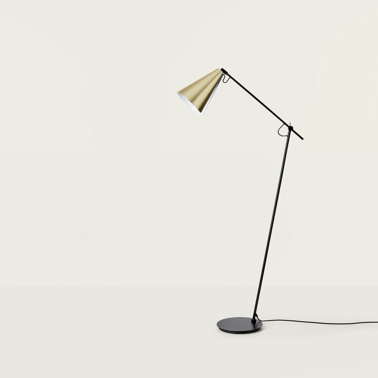La Lámpara de pie articulada Boa cuenta con un diseño moderno con un soporte negro, pantalla dorada en forma de cono y base redonda sobre un fondo liso, ofreciendo una iluminación ajustable para cualquier espacio.