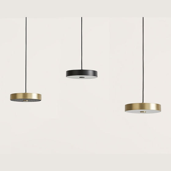 Tres luces colgantes cilíndricas con finos cables negros cuelgan del techo sobre un fondo blanco liso. La Lámpara de techo Ambor 3 x G9 se presenta en acabados dorado y negro, plasmando un diseño minimalista que proporciona iluminación dirigida a cualquier estancia.