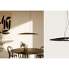 Interior de un comedor moderno con una mesa redonda, cuatro sillas, una lámpara de techo minimalista BigCoss que proporciona iluminación LED, arte abstracto en la pared y una pequeña planta en un jarrón sobre la mesa.
