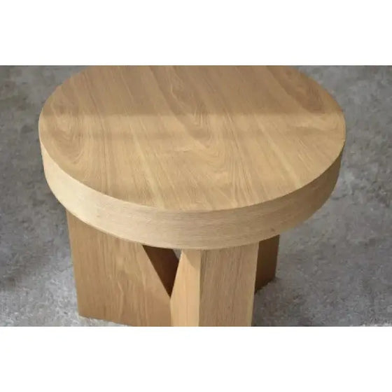 Mesa Auxiliar Fresno Natural Mocca - Triangulum redonda de madera, colocada sobre un suave suelo de moqueta.