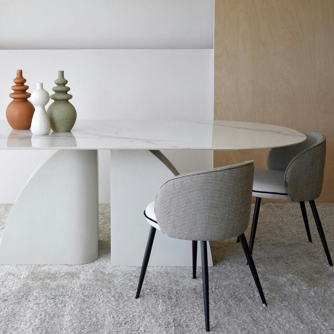 Un comedor moderno cuenta con una Mesa de Comedor Blanco-Gris Norte, acompañada de dos sillas tapizadas en gris y tres jarrones decorativos sobre la mesa, sobre un fondo minimalista con tonos neutros.