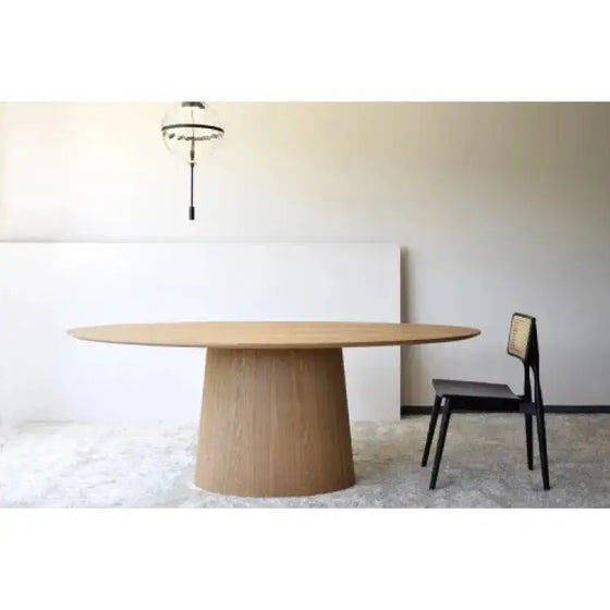 Una Mesa de Comedor Oval Fresno Natural - Abies con una silla negra delante.