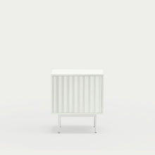  La mesita de noche Sierra 2C de Cambres Design es una mesa auxiliar minimalista blanca con un frente acanalado, una base de metal delgada y un fondo blanco liso para un almacenamiento elegante.