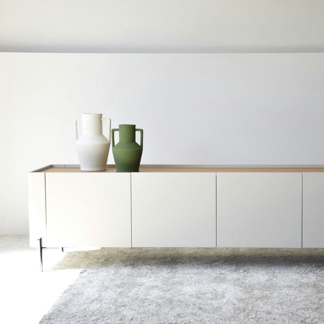 El Mueble TV Arena Mate y Roble Natural - Armonízate presenta un diseño minimalista con una cubierta de roble natural y un acabado lacado blanco mate, mostrando elegantemente dos grandes jarrones en blanco y verde sobre una alfombra gris claro, agregando una sutil sofisticación a su espacio vital.