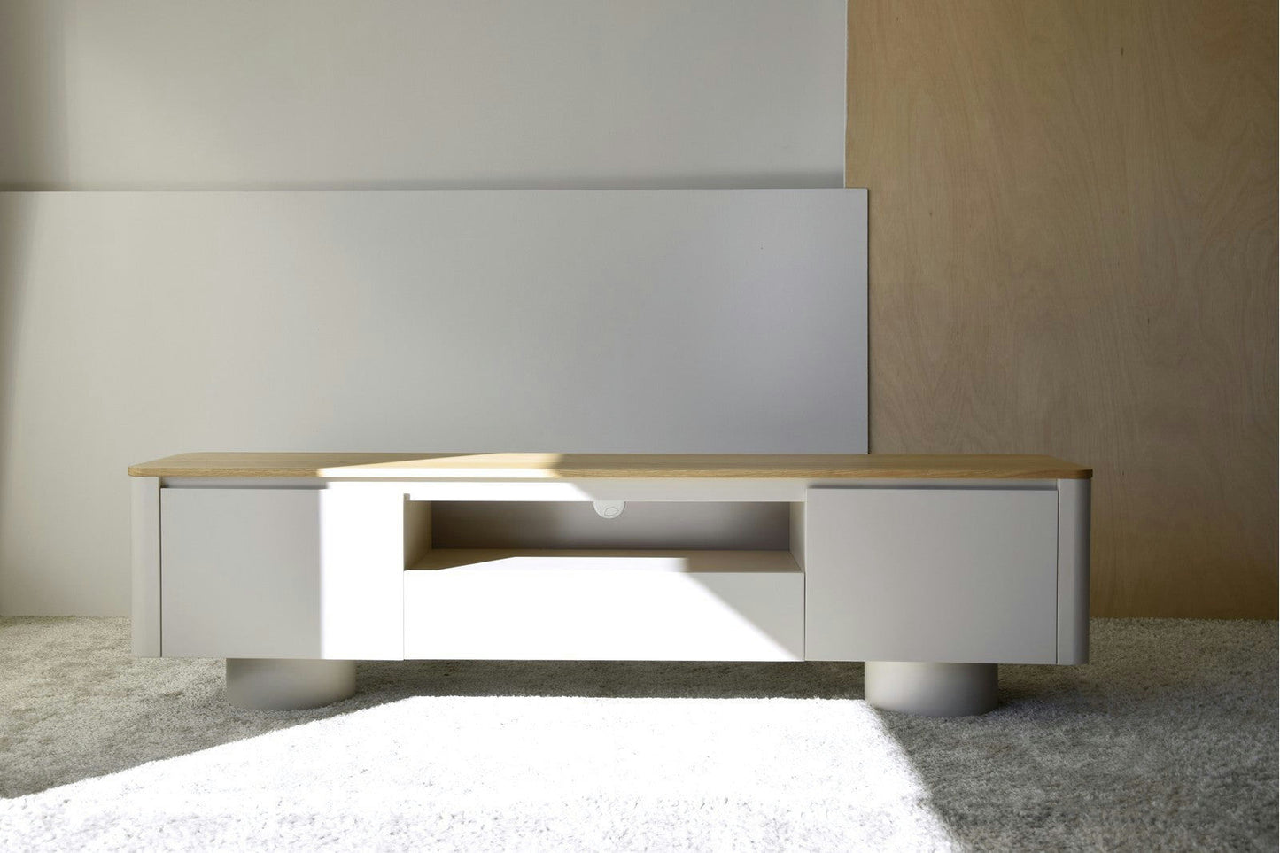 El Mueble TV Gris Arena y Roble Cilindro presenta una cubierta de madera clara con un cuerpo blanco, capturando un diseño minimalista. Ubicado sobre una alfombra en una habitación luminosa, sus estantes abiertos fusionan estilo y funcionalidad.