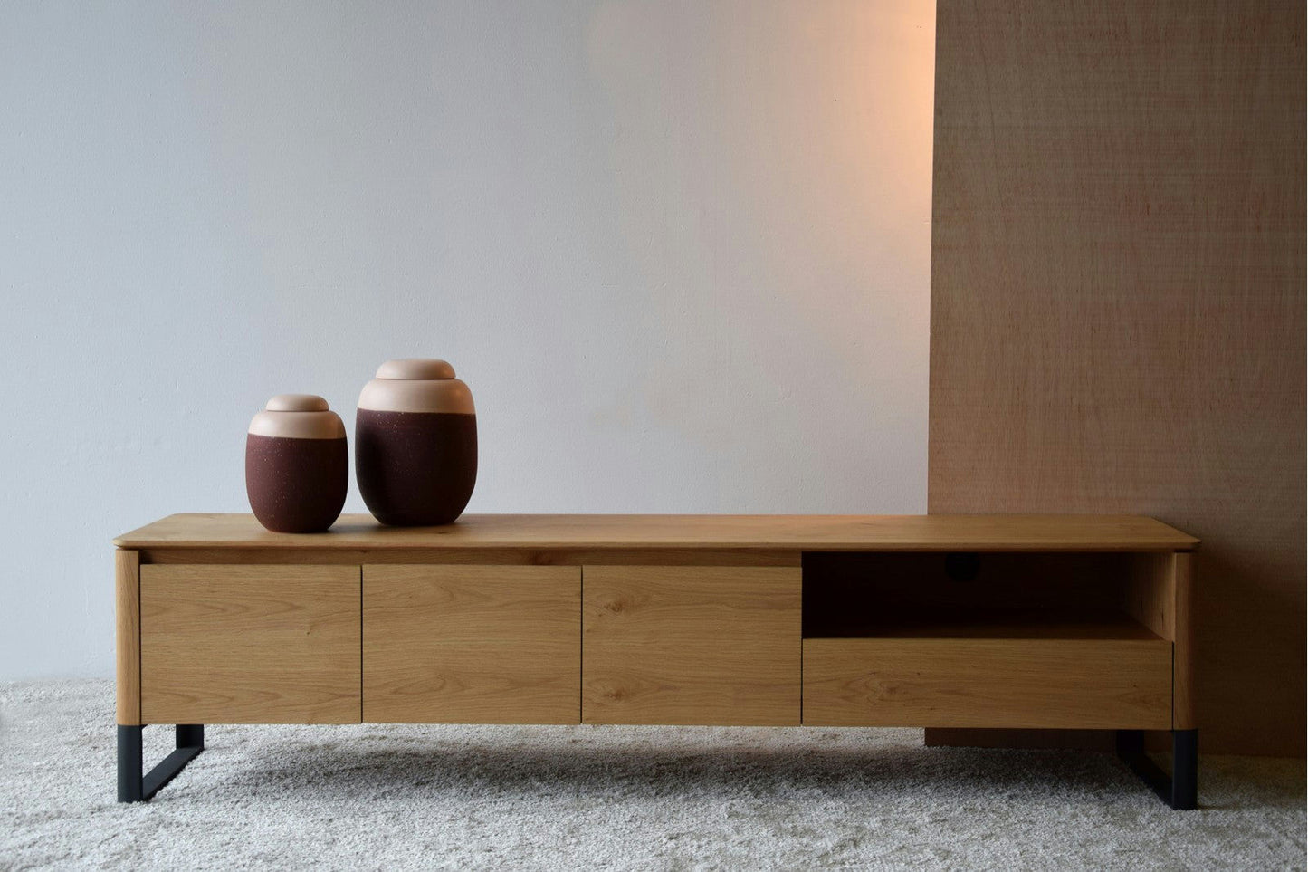 El Mueble TV Roble Natural Mate y Grafito - Lignar se encuentra hermosamente sobre una alfombra peluda con dos jarrones de cerámica marrón encima, sobre un fondo minimalista y elegante, que ofrece un almacenamiento elegante.
