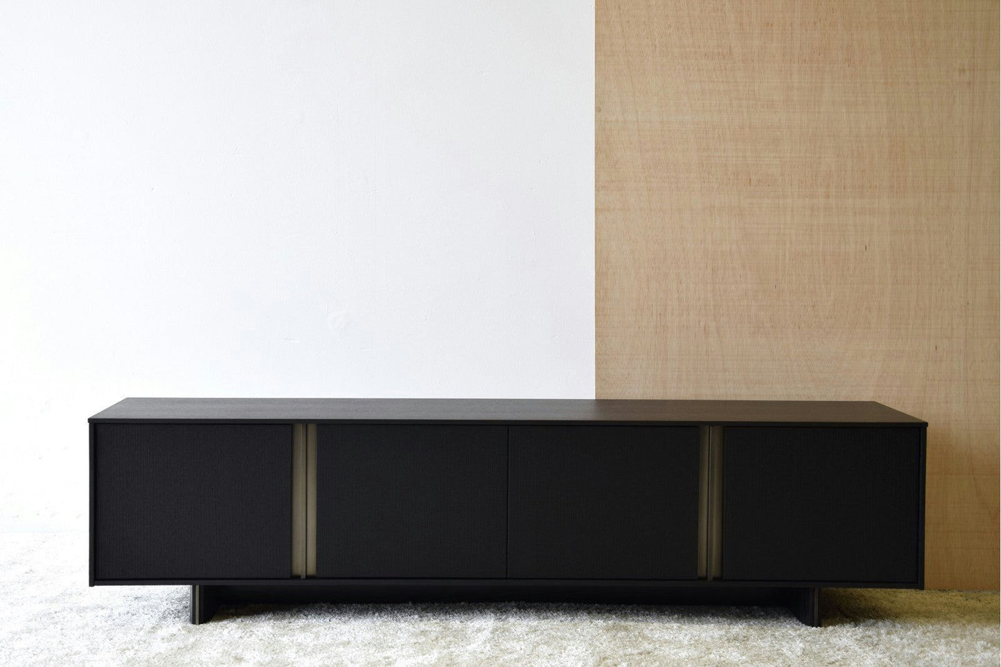 El Mueble TV Roble Negro Mate, con detalles en Oro Viejo, se destaca elegantemente contra una pared de dos tonos sobre una alfombra clara.