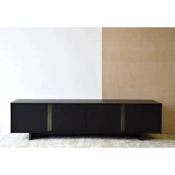 Un Mueble TV Roble Negro Mate, Detalles Oro Viejo frente a una pared blanca.