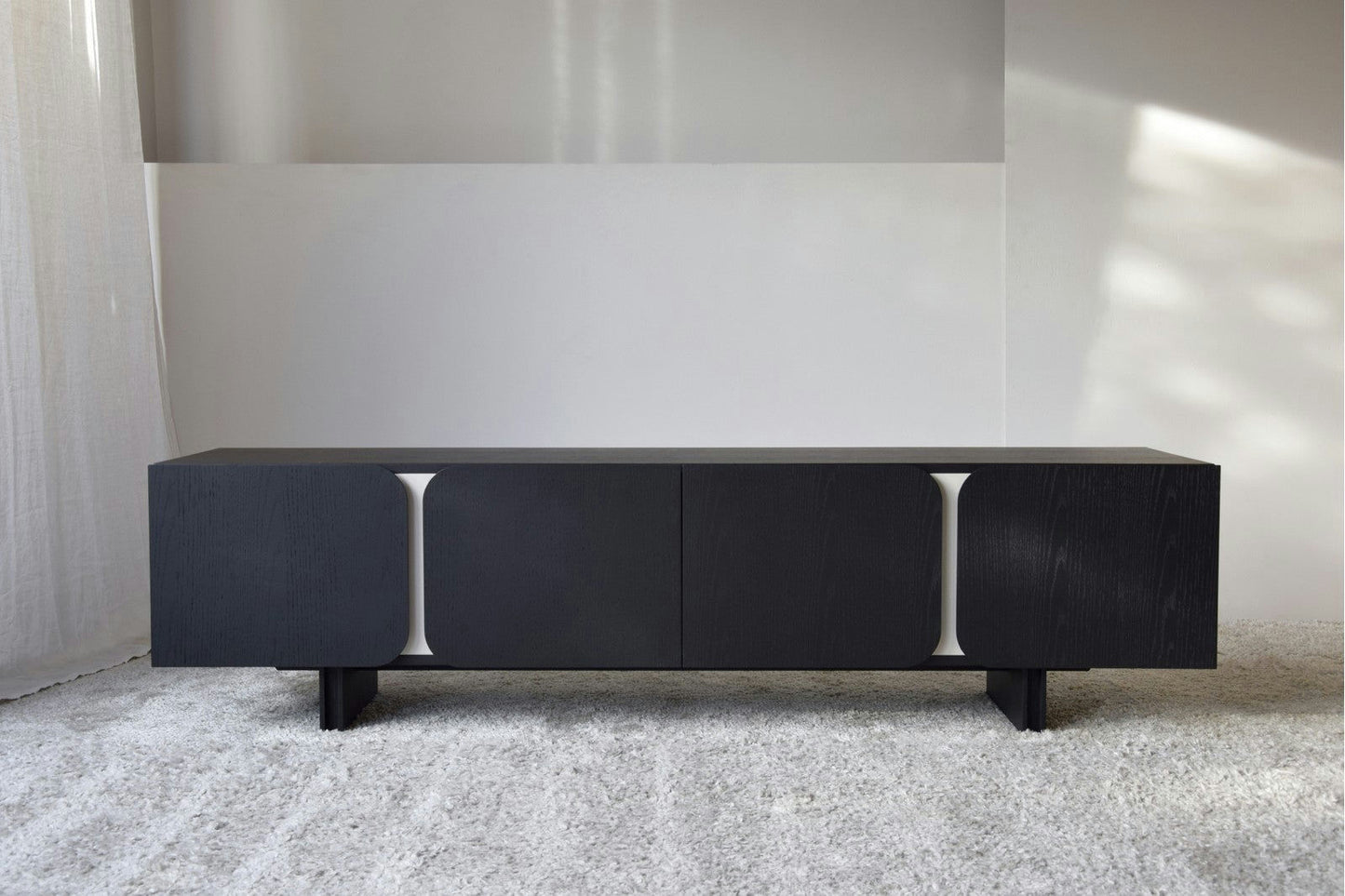 El Mueble TV Roble Negro mate Y Arena - Curva, con su diseño elegante y contemporáneo, se asienta elegantemente sobre un piso alfombrado claro.