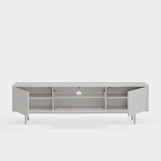 Mueble TV Sierra 3P de perfil bajo y diseño modernista en color gris claro, con cuatro compartimentos abiertos que muestran estantes interiores y un orificio circular.