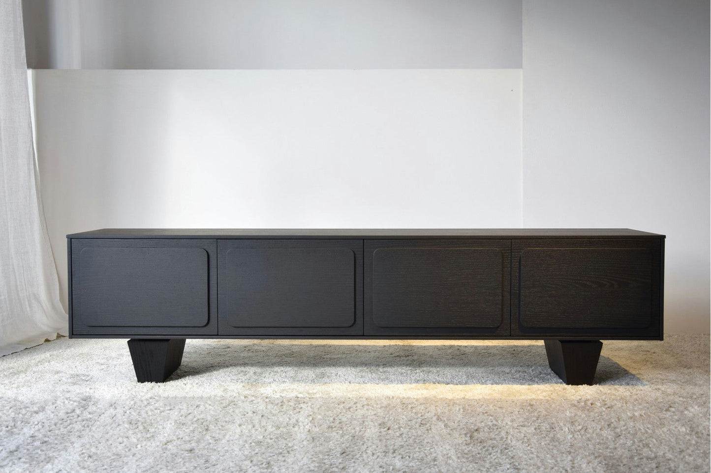 Un elegante aparador llamado "Mueble TV en Roble Teñido Negro - Río" con puertas de cuatro paneles se encuentra sobre una alfombra clara en una habitación minimalista, mostrando su impecable diseño de sistema "push".