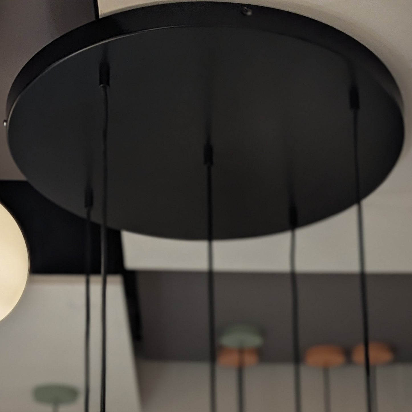 Primer plano de la lámpara colgante en acero negro S-Toru 3: un colgante circular negro con múltiples cordones, fabricado en acero, que presenta un moderno diseño industrial sobre un fondo suavemente difuminado.