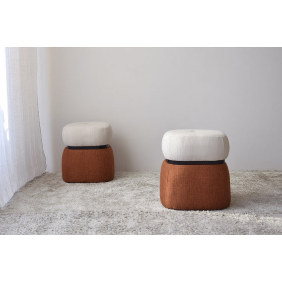 Two Pack 2 Puffs Cuadrados Tapizados Teja con bases marrones y tapas blancas se asientan sobre una alfombra de color claro junto a una cortina en una habitación minimalista, añadiendo un toque contemporáneo al diseño elegante.