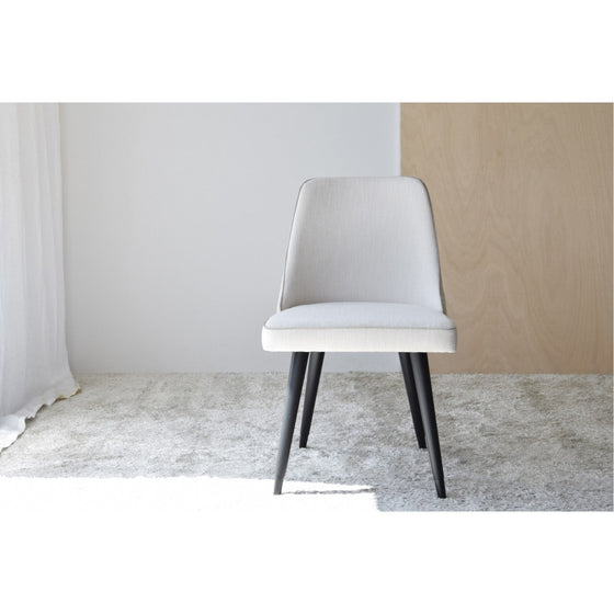 Un Pack de 2 Sillas de Comedor en Tonos Beige - Comodante minimalista y tapizado con patas de madera oscura se asienta sobre una alfombra clara en una habitación luminosa con paredes blancas y de madera, mostrando elegancia moderna.