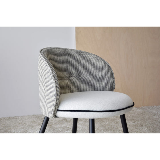 Una silla moderna con un asiento acolchado de color gris claro, un respaldo tejido de color gris y patas de metal negro se asienta elegantemente sobre una alfombra beige y negra, complementada con un panel de madera clara en el fondo. Perfecto para ambientes Pack 2 Sillas de Comedor Tapizadas Envogué.