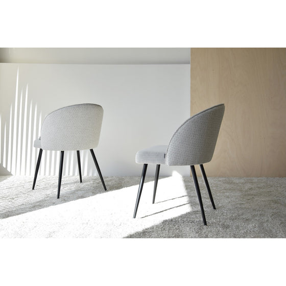 Un paquete de Pack 2 Sillas de Comedor Tapìzadas Sofistica en gris claro, con elegantes patas de metal negro, se asienta elegantemente sobre un piso alfombrado claro contra un fondo minimalista con iluminación natural.