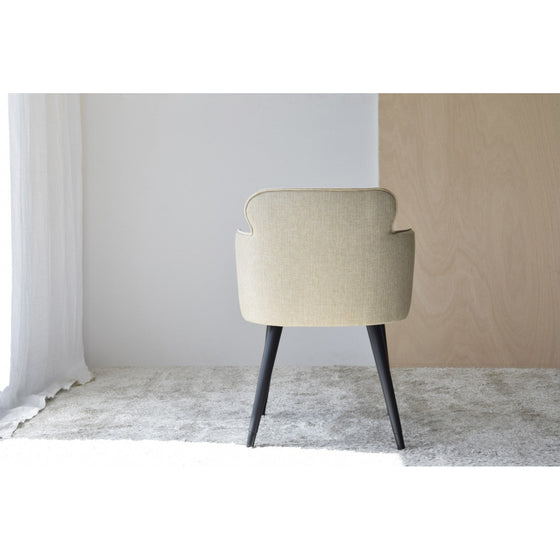 Un par de sillones beige naturales inspirados en Oslo con patas negras están colocados contra una pared blanca y un panel de madera, sobre una alfombra gris claro. La luz se filtra a través de una cortina transparente a la izquierda en este ambiente elegante.