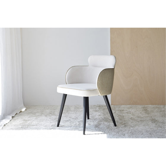 Una moderna silla tapizada con tela natural beige y patas negras se asienta sobre una alfombra gris claro en una habitación con paredes blancas y un panel de madera. Este Pack de 2 Sillas de Comedor con Brazos Oslo añade un toque de elegancia a cualquier espacio de comedor.