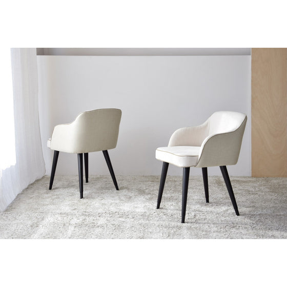 Two Pack 2 Sillas de Comedor con Reposabrazos Elysare con patas de madera oscura se colocan sobre una alfombra de color claro en una habitación minimalista. Una silla mira hacia adelante, mientras que la otra está ligeramente inclinada hacia la derecha, mostrando su diseño cómodo.