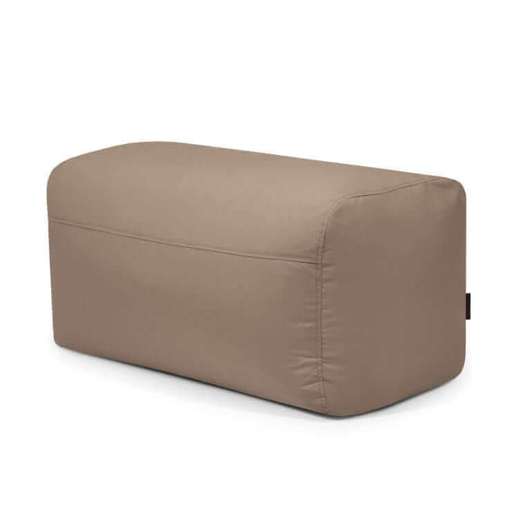 El Pouf Plus 100 Colorin - uso exterior es una otomana rectangular de tela de color topo con bordes redondeados que sirve de asiento ergonómico, mostrada sobre fondo blanco.