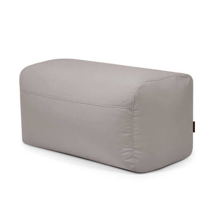 El Pouf Plus 100 Colorin - uso exterior es un puf rectangular de tela gris claro con bordes redondeados que ofrece un elegante asiento ergonómico para espacios exteriores, sobre fondo blanco.