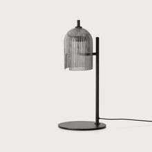  Lámpara de mesa Porta moderna con pantalla semitransparente acanalada verticalmente y un elegante soporte negro que ofrece una iluminación eficiente sobre un fondo liso.