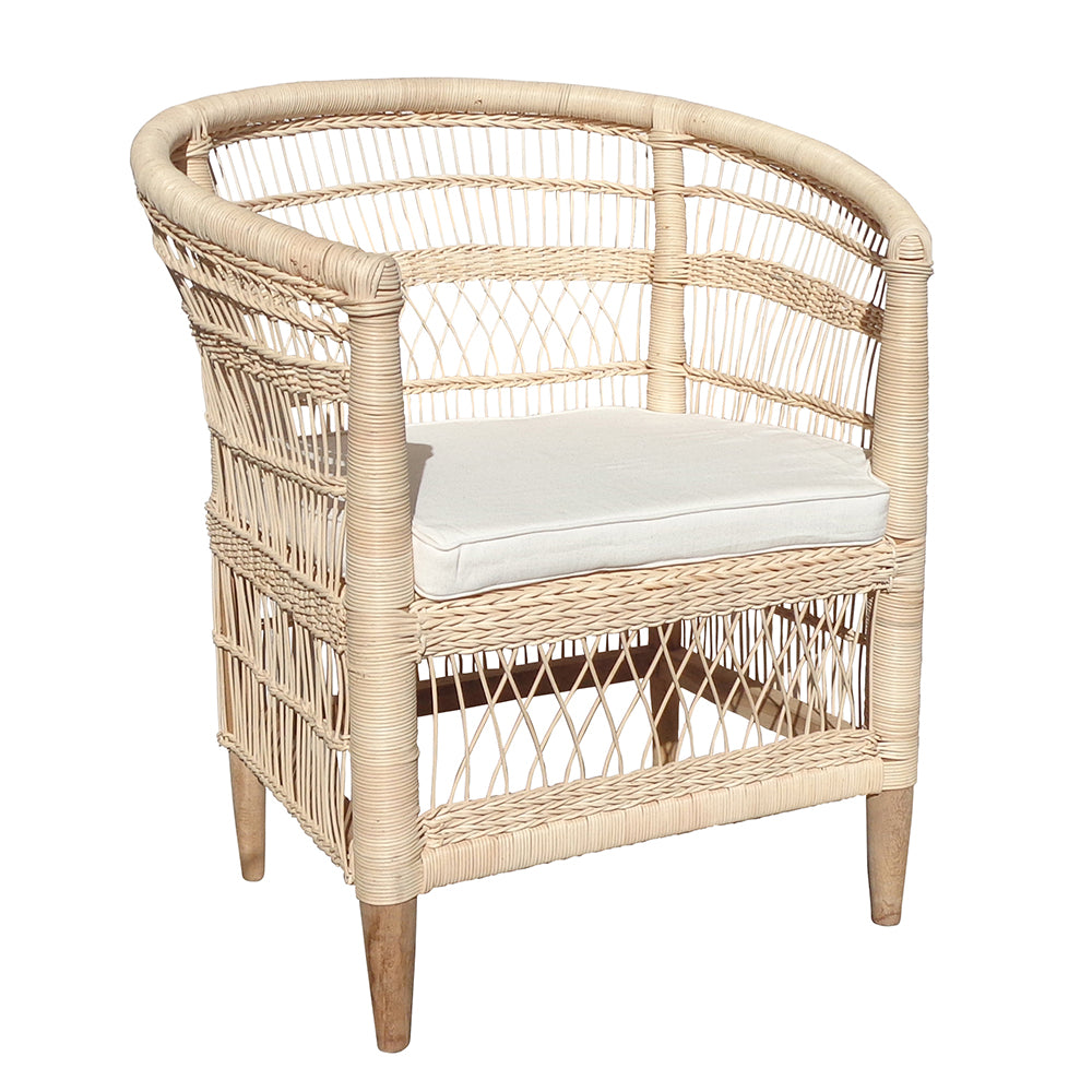La Butaca en ratán con Cojín Majaro destaca por su respaldo curvo, laterales abiertos tejidos, cojín blanco y cuatro patas de madera, combinando diseño moderno y materiales naturales.