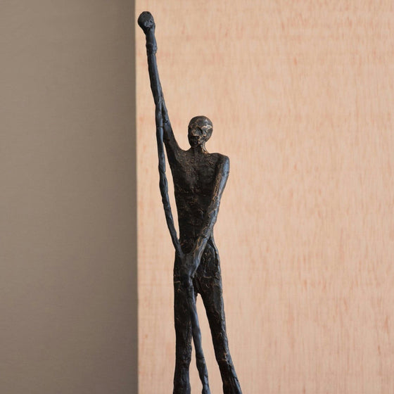 La Figura decorativa de metal en bronce envejecido Hombre N4 destaca como una escultura esbelta y alargada con un brazo levantado contra la pared de color claro, que encarna a la perfección el diseño minimalista y complementa cualquier decoración moderna.