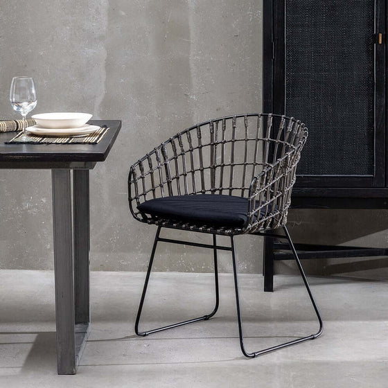 Espacio de comedor moderno con una silla Silla Graphite-Ratan en Gris-Negro y una mesa de madera oscura con platos y cristalería, que incorpora ratán de alta calidad en su moderna decoración interior.
