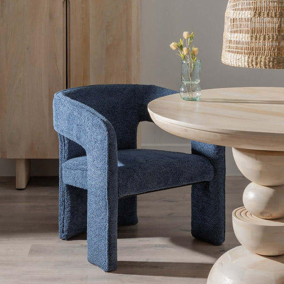 Moderna Silla Nimbus Azul de tela azul junto a una mesa redonda de madera con un jarrón de flores, en una habitación de Diseño Contemporáneo.