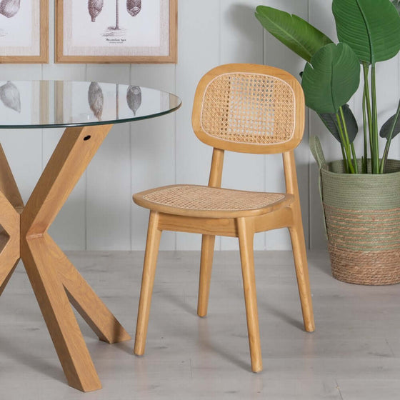 Silla Nordic Elm Natural en Madera de Olmo con asiento y respaldo de ratán tejido en una habitación moderna con una mesa de vidrio y planta en maceta.