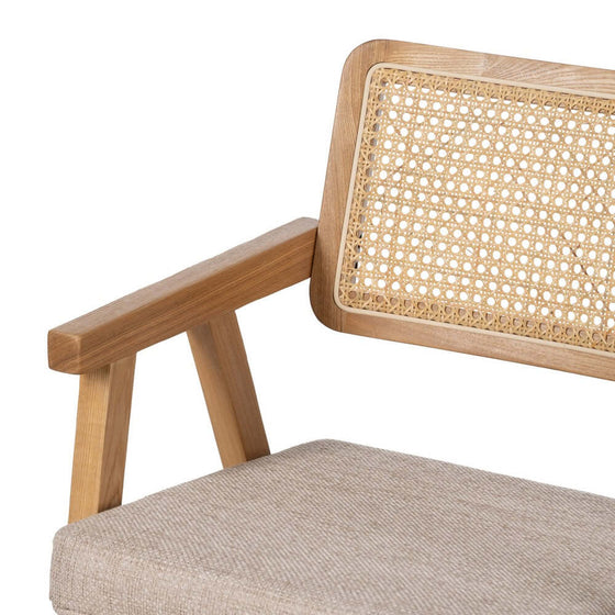 Primer plano de una Silla Nórdika Essence con Brazos hecha de madera de haya con correas de caña y un cojín beige, reflejando el diseño escandinavo.