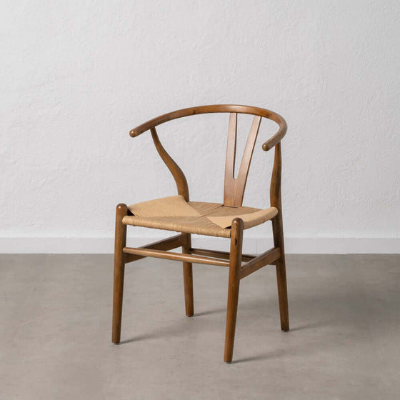 Una Silla Scandbone Marrón en Madera de Abedul con asiento tejido contra una pared blanca sobre un suelo gris.