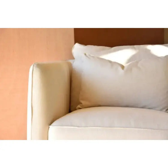 Un cómodo Sillón Cuadrado en Lino Beige con una elegante almohada frente a una pared beige.