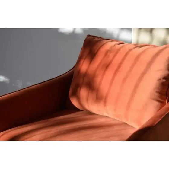 Un sillón rojo oscuro cuadrado de diseño interior contemporáneo con un cojín de terciopelo colocado frente a una ventana.